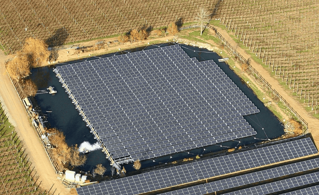 An array of solar panels sits on a small body of water.